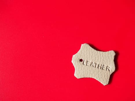 A sample of genuine leather for shoes, haberdashery, bags, gloves, upholstery of furniture. Beige or gray material on a red background. Copy space. Natural or artificial leather for sewing products