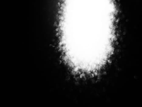 White bokeh and beam on a black background. Blurred glow from above on a dark surface. Night or space theme. Bokeh for the holiday. Association for a flying meteorite. Abstract theme.