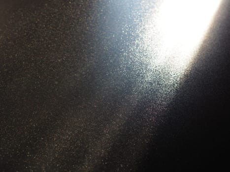 Abstract black background. Oblique light rays on a black blackdrop with flickering dots. From right top, the lines are directed down and to the left. Glow, flare or shine. Side lighting. Small glow.