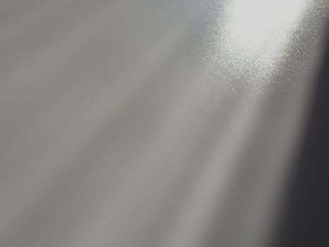 Diagonal rays of light on a gray background. Blurred abstract background light effect, light leaks. Side surface illumination. Small sparks and glow. Shine, glint or glare. Right top left down.