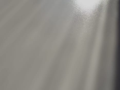 Diagonal rays of light on a gray background. Blurred abstract background light effect, light leaks. Side surface illumination. Small sparks and glow. Shine, glint or glare. Right top left down.