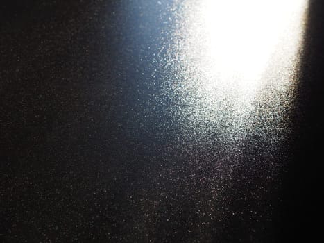 Abstract black background. Oblique light rays on a black blackdrop with flickering dots. From right top, the lines are directed down and to the left. Glow, flare or shine. Side lighting. Small glow.