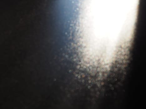 White bokeh and beam on a black background. Blurred glow from above on a dark surface. Night or space theme. Bokeh for the holiday. Association for a flying meteorite. Abstract theme.