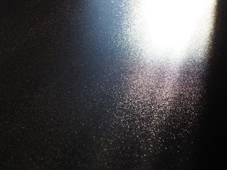 Abstract black background. Oblique light rays on a black blackdrop with flickering dots. From right top, the lines are directed down and to the left. Glow, flare or shine. Side lighting. Small glow.