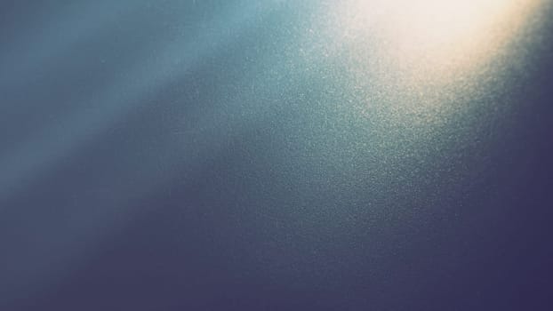 Oblique ray of light on a blue background. Blurred abstract backdrop with light effects and leaks. Side surface illumination. Divergent and asymmetric lines, stripes of light at angle. Yellowish glow