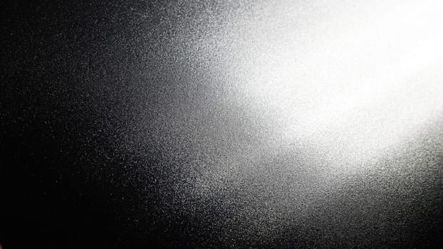 White bokeh and beam on a black background. Blurred glow from above on a dark surface. Night or space theme. Bokeh for the holiday. Abstract background. Glare, ray and light shine from above.