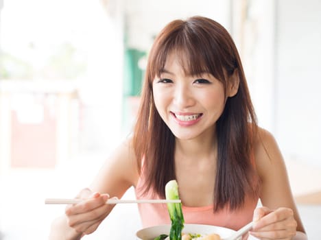 Asian girl eating vegetable noodles at Chinese restaurant. Young woman living lifestyle.