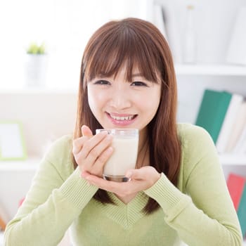 Portrait of happy Asian girl drinking soy milk as breakfast. Young woman indoors living lifestyle at home.