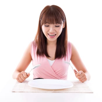 Asian girl holding fork and spoon with surprised expression, empty plate ready for food. Young woman living lifestyle.