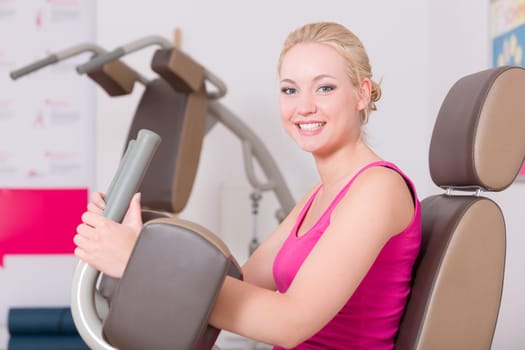 A young pretty woman in a pink shirt doing exercises in a gym