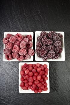 Three varieties of frozen berry fruits in porcelain bowls