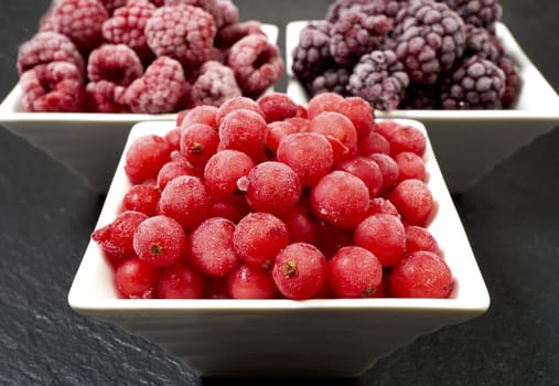 Three varieties of frozen berry fruits in porcelain bowls