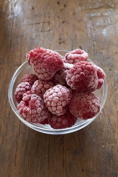 Frozen raspberries in a glass bowl on a wooden table