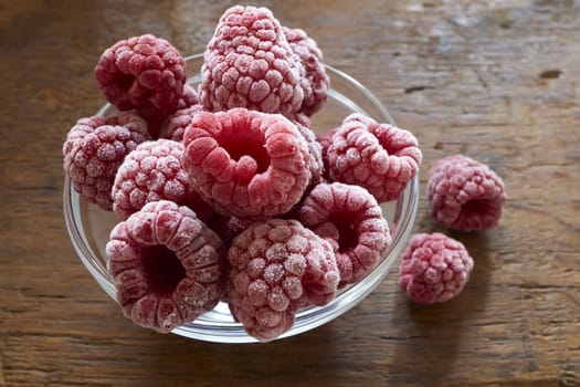 Frozen raspberries in a glass bowl on a wooden table