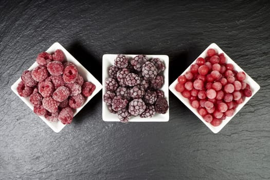 Three varieties of frozen berry fruits in porcelain bowls