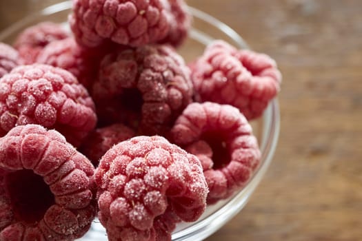 Frozen raspberries in a glass bowl on a wooden table