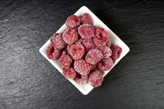 Frozen raspberries in porcelain bowl on slate plate