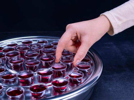Closeup of young woman taking communion the wine symbol of Jesus Christ blood in small cups on black background. Easter Passover and Lord Supper concept.