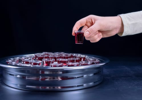 Closeup of young woman taking communion the wine symbol of Jesus Christ blood in small cups on black background. Easter Passover and Lord Supper concept.