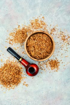 Dry smoking tobacco and a smoking tube or pipe on a gray background