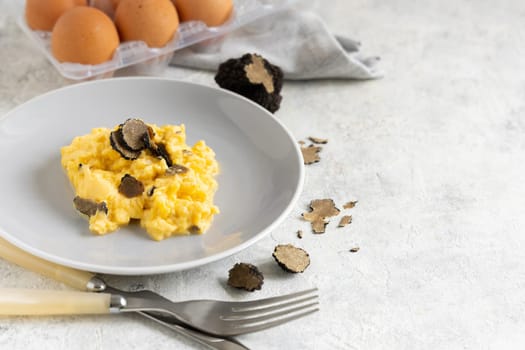 Scrambled eggs with sliced fresh black truffles from Italy served in a plate near fork and knife close up, copy space. Italian cousine, gourmet breakfast