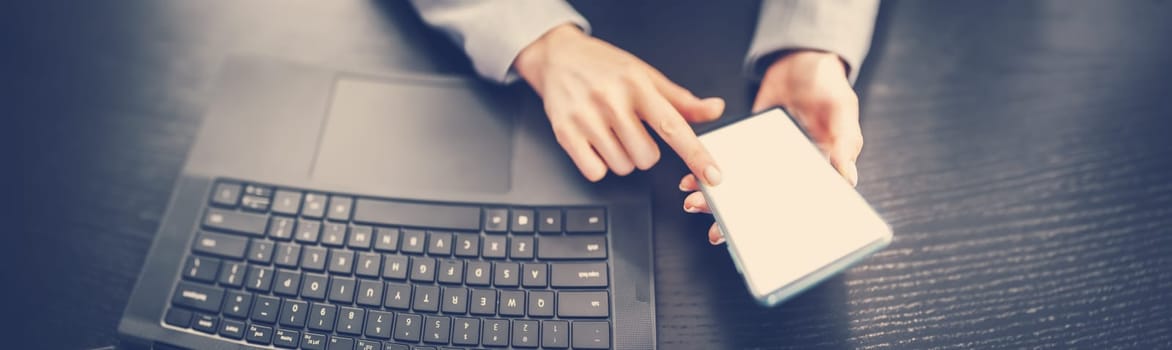Woman holding in her hands mobile phone and typing on the laptop. Concept of the e-commerce, business and surfering in network.