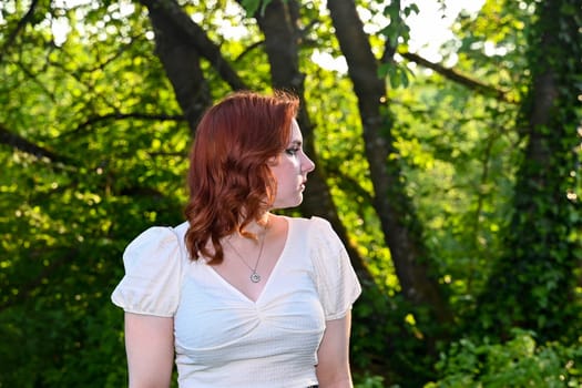 Portrait of a young redhead girl in green nature, looking to the side