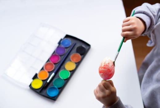 Close up of childrens hands holding easter egg and painting it with a brush at home. Preparation for easter. Happy easter. High quality photo.