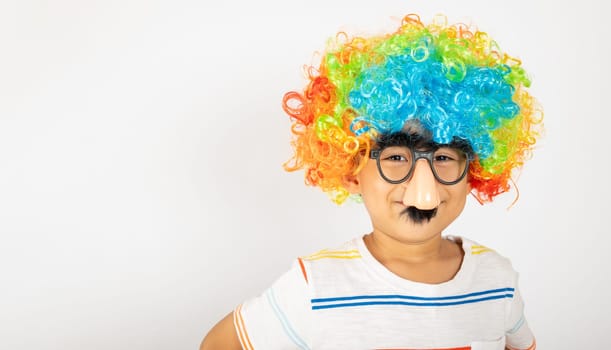 April Fool's Day. Portrait of Funny kid boy clown wears a curly wig colorful a big nos and glasses and has a mustache isolated on white background with copy space, Happy child festive decor