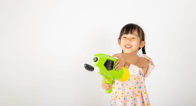 Happy Songkran Day, Asian little girl holding plastic water gun, Thai child funny hold toy water pistol and smile, isolated on white background, Thailand Songkran festival national culture concept