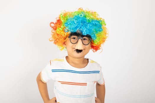 April Fool's Day. Portrait of Funny kid boy clown wears a curly wig colorful a big nos and glasses and has a mustache isolated on white background with copy space, Happy child festive decor