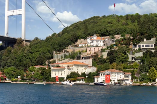 View from the sea of the Asian side of Bosphorus strait, Istanbul, Turkey, with traditional waterfront houses, under Bosphorus bridge, and green hill with dense trees, in a summer day