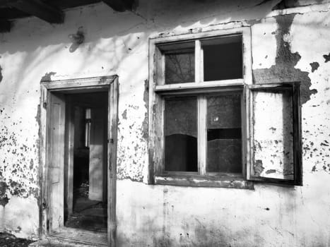 Old house with windows and a door. Collapsing rural house. The concept of urbanization and oblivion of the motherland. Abandoned house. Broken glass in the window and falling plaster. Serbia. Balkans.