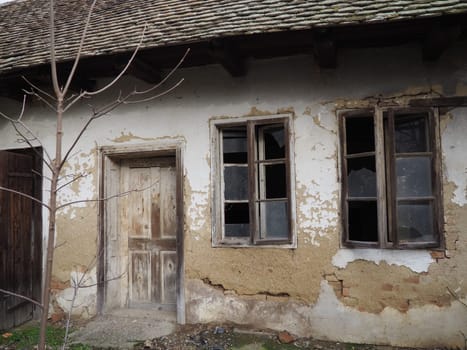 Old house with windows and a door. Collapsing rural house. The concept of urbanization and oblivion of the motherland. Abandoned house. Broken glass in the window and falling plaster. Serbia. Balkans.