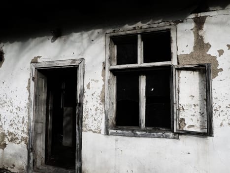 Old house with windows and a door. Collapsing rural house. The concept of urbanization and oblivion of the motherland. Abandoned house. Broken glass in the window and falling plaster. Serbia. Balkans.