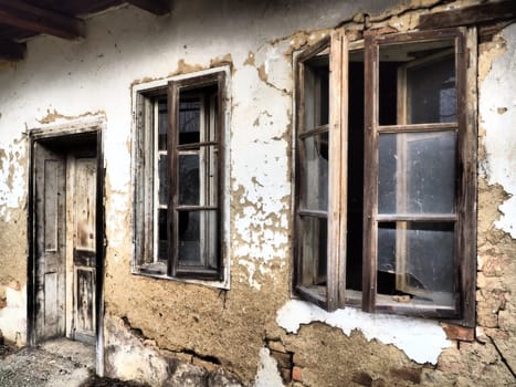 Old house with windows and a door. Collapsing rural house. The concept of urbanization and oblivion of the motherland. Abandoned house. Broken glass in the window and falling plaster. Serbia. Balkans.