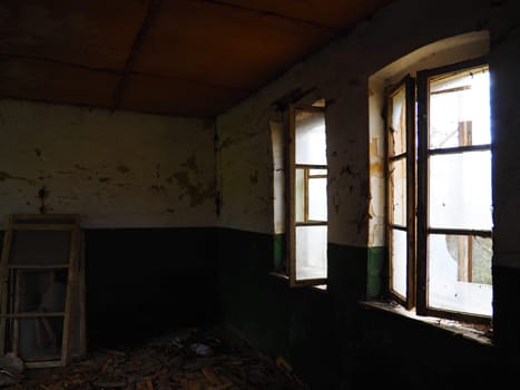 Scary windows. Inside an abandoned house. View of broken windows without a curtain. Grunge scene. Light shines through old wooden frames with broken glass. The concept of abandonment and uselessness.