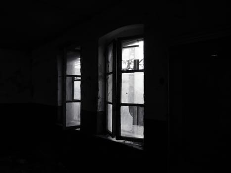 Scary windows. Inside an abandoned house. View of broken windows without a curtain. Grunge scene. Light shines through old wooden frames with broken glass. The concept of abandonment and uselessness.