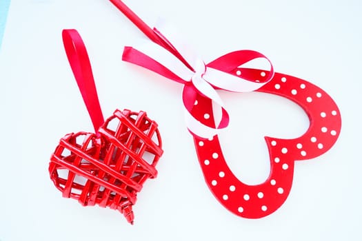 Valentine's day concept. Two red hearts. Wooden heart with white dots and a ribbon bow on a stick. Wicker heart with a loop. White background. Flat lay.
