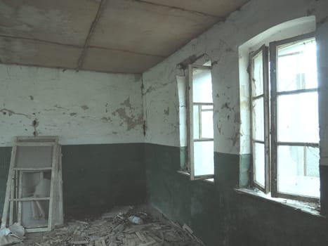 Scary windows. Inside an abandoned house. View of broken windows without a curtain. Grunge scene. Light shines through old wooden frames with broken glass. The concept of abandonment and uselessness.