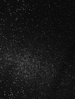 Black bokeh texture on black background. White glitter or illuminated dust.