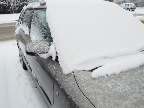Snow and ice on the windshield, retrovisors and rear-view mirrors of the car. Winter driving conditions. Snow cleaning. Road traffic in winter. Metallic car. Snowdrifts and slush