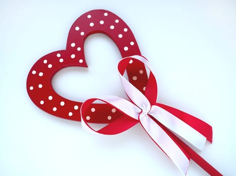 Valentine's day concept. Red wooden heart with white dots and ribbon bow on a stick. White background. A beautiful bow as a decoration. Love and relationships. Recognition or congratulations.