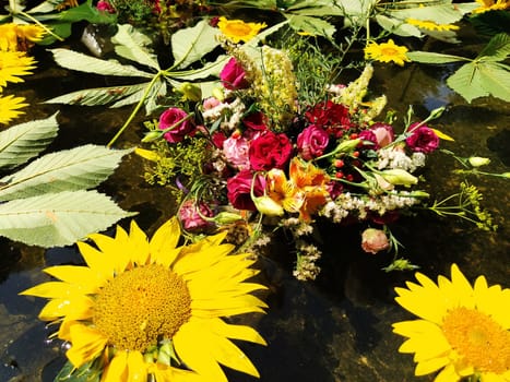 Yellow decorative sunflowers, pink and red roses in a bouquet floating in the water of a fountain. Plucked buds as decoration for a summer holiday. Ivan Kupala, summer solstice. Harvest festival