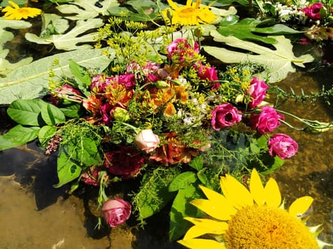 Yellow decorative sunflowers, pink and red roses in a bouquet floating in the water of a fountain. Plucked buds as decoration for a summer holiday. Ivan Kupala, summer solstice. Harvest festival