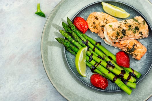 Healthy lunch of trout, asparagus and tomato on a wooden table.