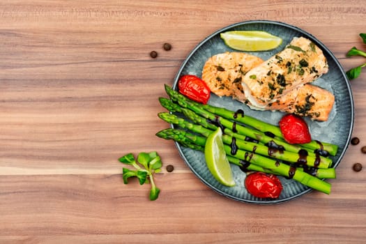 Healthy lunch of trout, asparagus and tomato on a wooden table.