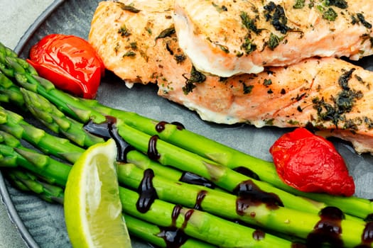 Healthy lunch of trout, asparagus and tomato on a wooden table.