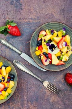 Salad of pineapple, strawberries and berries with edible flowers in a bowl