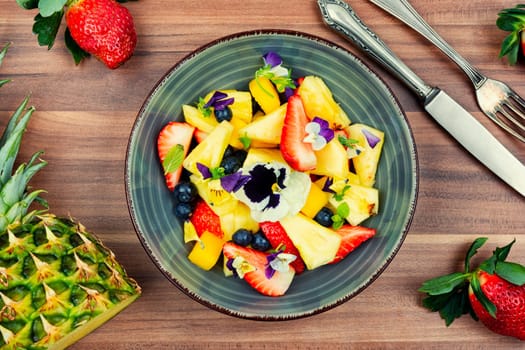 Salad of pineapple, strawberries and berries with edible flowers in a bowl